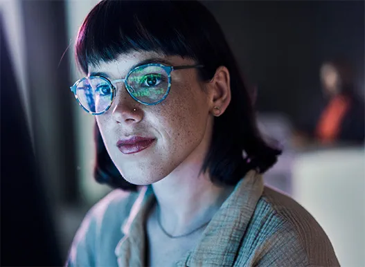 A woman with glasses with reflection of a computer screen on them.